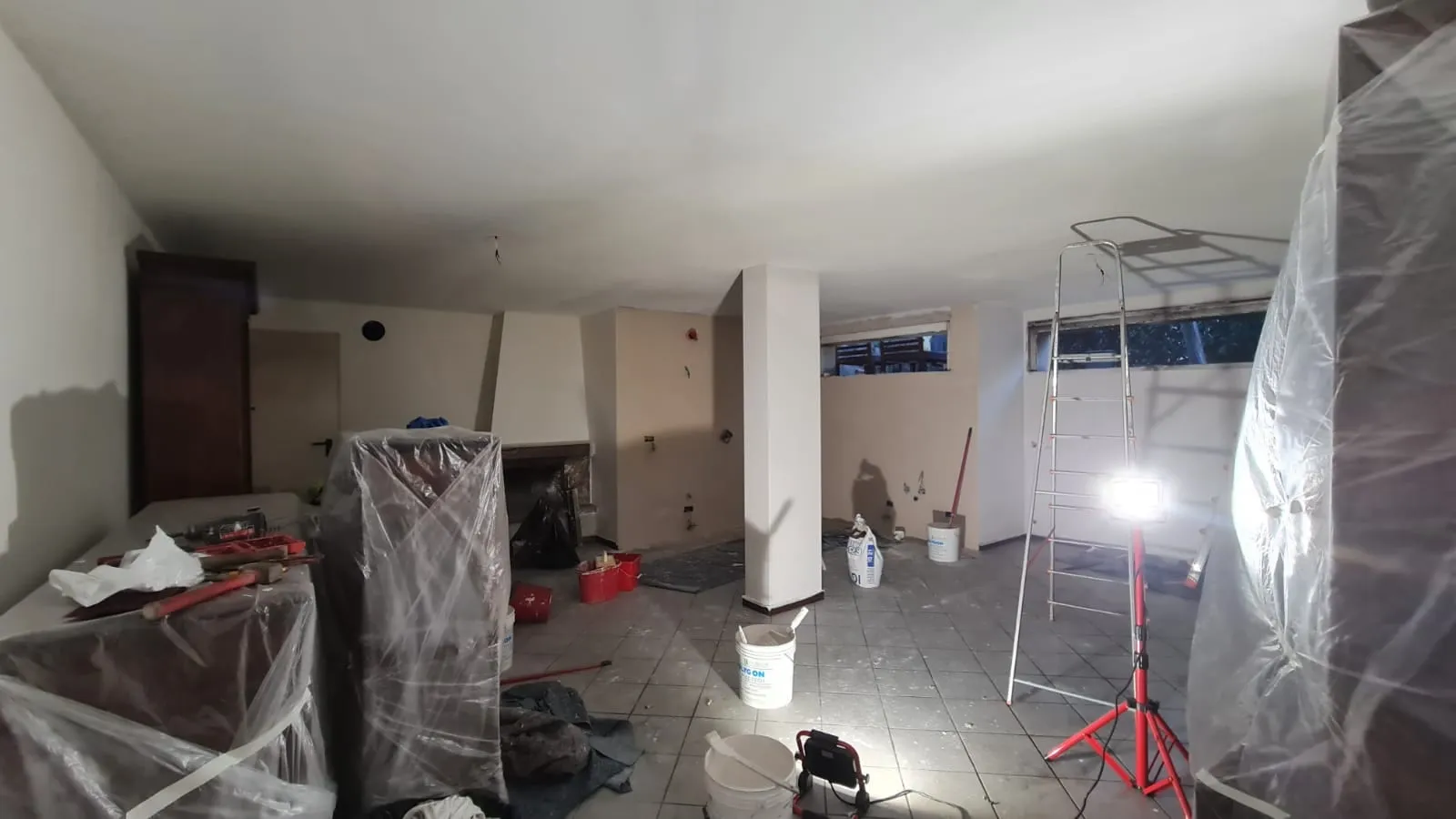 Ambiente in fase di bonifica e ripristino, con arredi protetti e faro da lavoro